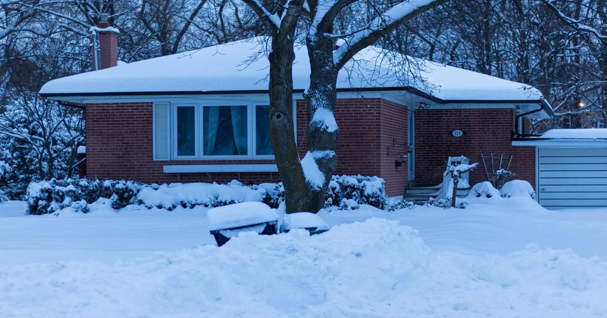 Maison de plain-pied enneigée dont le toit en pente porte une épaisse couche de neige